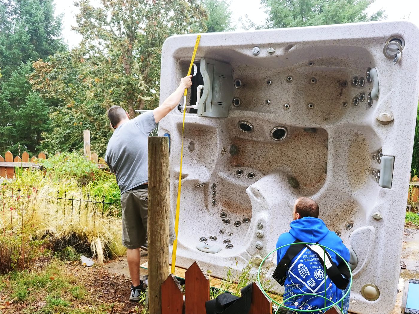 Crew tipping a hot tub on its side to move it through a narrow side yard